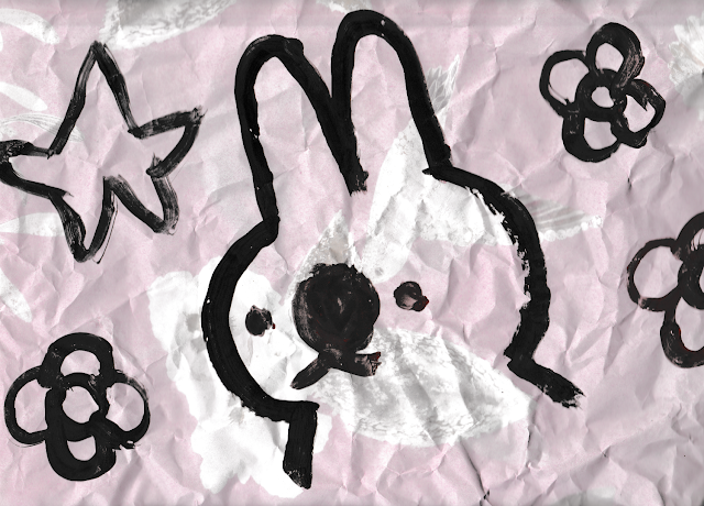 A painting of a bunny surrounded by three flowers and a star on crumpled pink paper.