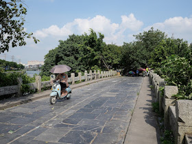 Person holding umbrella while riding a motor scooter on Yunlong Bridge (云龙桥) in Yulin