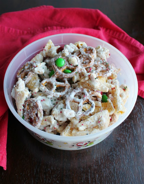 This fun sweet and salty snack mix only takes a few minutes to make and the results are delicious. This version is decked out in red and green for the merriest of white trash snack goodness, but the colors could easily be changed for any occasion. container of sweet and salty white chocolate trash Christmas snack mix ready to be gifted