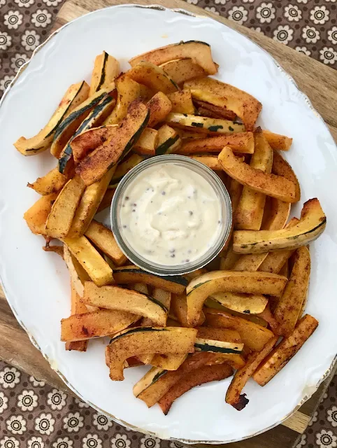 Finished roasted delicata squash sticks on a platter with a dish of creamy maple mustard dipping sauce.
