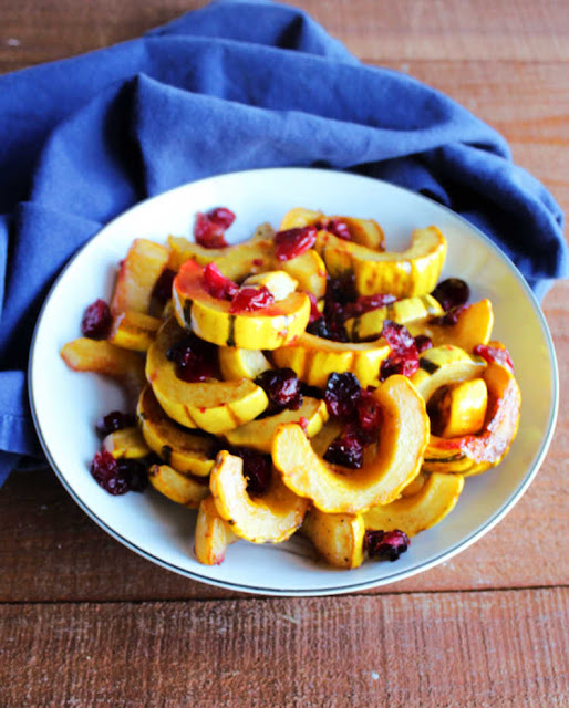 The perfect fall side dish has arrived! The combination of roasted delicata squash and cranberries lightly glazed with orange and honey will make your dinner plate sing! bowl of roasted slices of delicata squash and cranberries