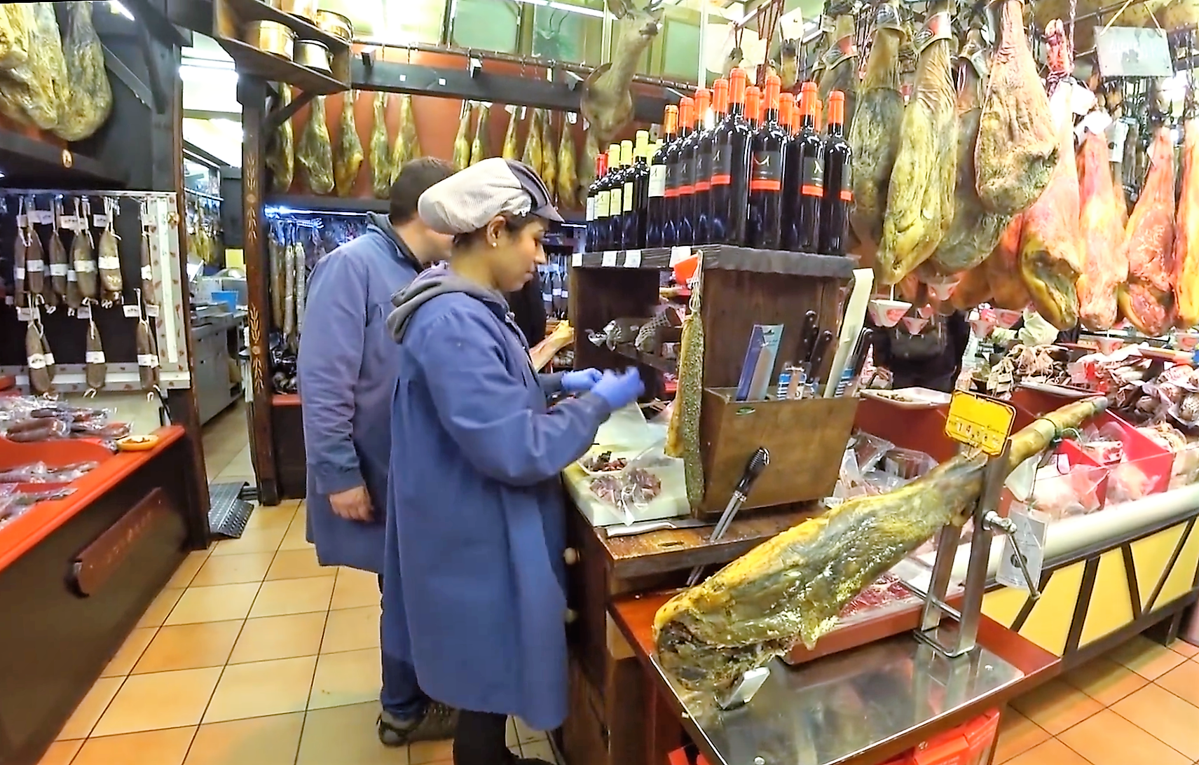 Food sellers in a meat market with big pieces of ham hanging
