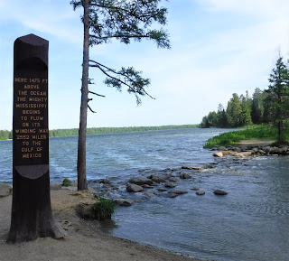 a pillar with information stands to the left of the headwaters of the Mississippi at Itasca State Park in Minnesota
