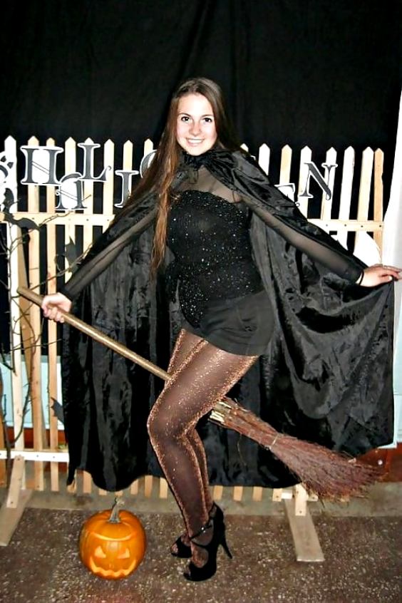 Sweet woman on a broom wearing black shorts, brown shiny tights and black peep toe high heels