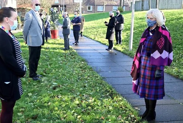 Duchess of Cornwall is wearing a face-mask and protective glasses. The Duchess wore a tartan coat dress, and a printed pattern scarf from Seasalt