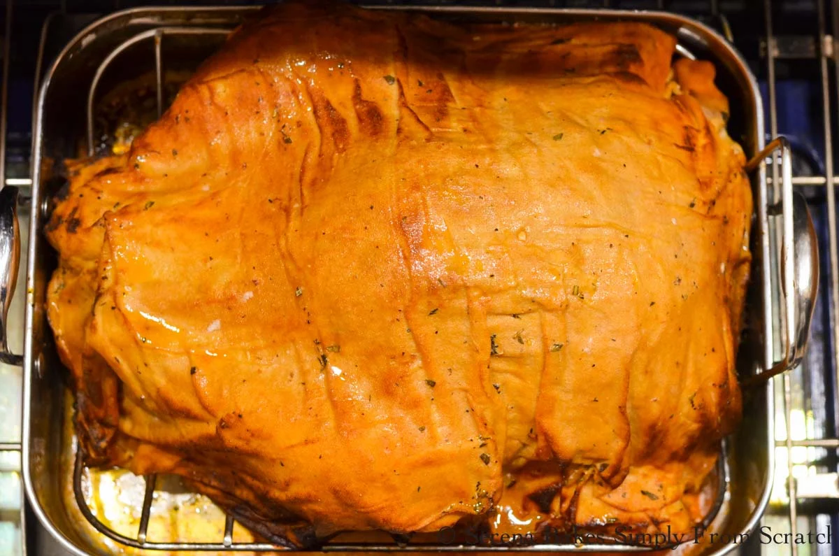 Cheesecloth covering turkey is brown from baking in the oven in a roasting pan.