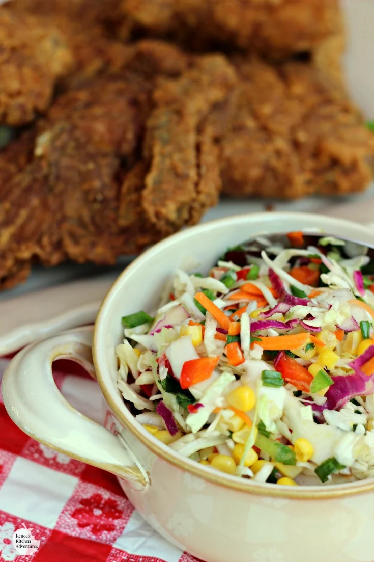 Firecracker Coleslaw by Renee's Kitchen Adventures close up in a bowl with fried chicken on a white platter in background