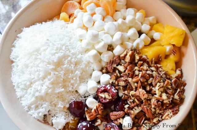 Ambrosia Fruit Salad Recipe in a bowl with fresh pineapple, mandarin oranges, cherries, coconut, pecans from Serena Bakes Simply From Scratch.