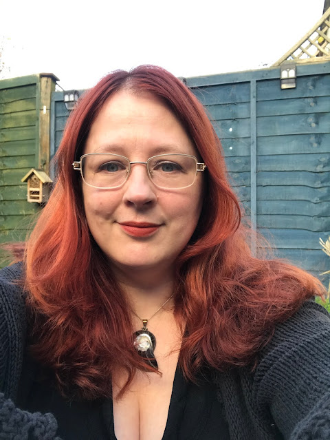 A close up of the face of a woman with red hair. She is smiling into the camera.