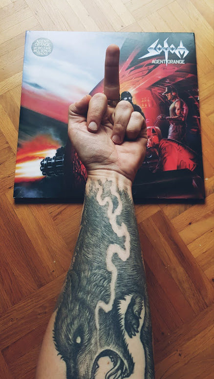 Tättovierter Unterarm mit Wolfstattoo mit ausgestrecktem Mittelfinger zur Sodom Vinyl "Agent Orange"