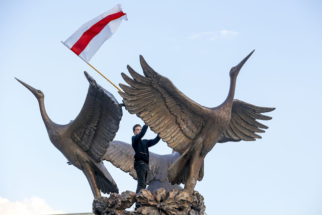 A demonstrator waves an old Belarusian national flag atop the Fountain of Independence in Minsk