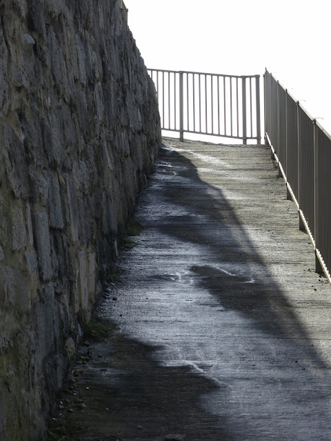 Concrete slope between stone wall and metal railings.