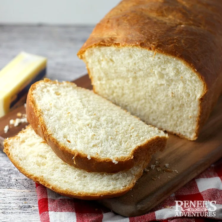 Soft White bread sliced from loaf laying over a wooden board with butter on the side