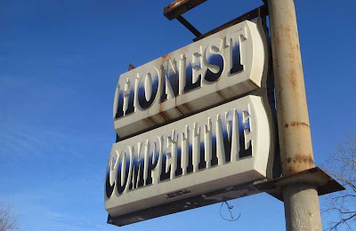 Lit plastic sign, faded by sun, with two words: HONEST COMPETITIVE