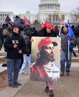 Protesters in front of U.S. Capitol, including woman in MAGA hat carrying poster with Jesus in a MAGA hat