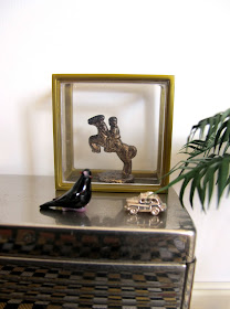 Art deco style modern miniature silver sideboard with a display case containing a horse and rider statue, and a glass bird and silver car ornament displayed in front of it.