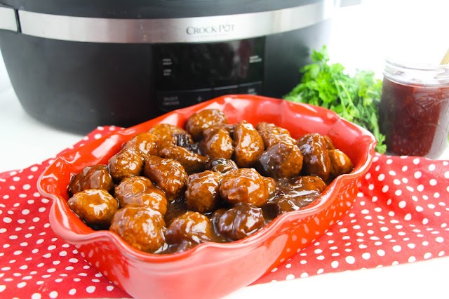 meatballs in a red casserole dish with a slow cooker in the background.