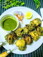 Serving hariyali kabab with shewer in a plate green chutney, onion slices, lemon wedges in background