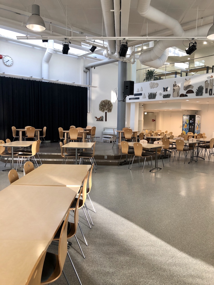 Salon seudun ammattiopiston Hyvoninkadun toimipisteen ruokala. Kuvassa on vaaleanpuunsävyisiä pöytiä ja tuoleja eri tasoissa, harmaa lattia sekä tyhjähköt seinät.