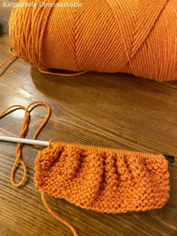 An orange knitted rectangle on a needle