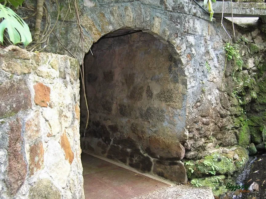 Detalhe do muro de pedra com o pórtico de pedra ligando uma passagem para o outro lado da residência.
