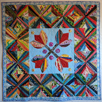 Four string tulips form an X in the center surrounded by a border of X string blocks in multicolors.