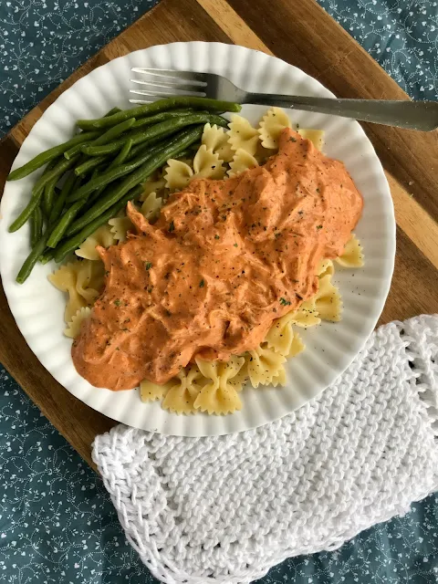 Plate of pasta topped with slow cooker creamy chicken and tomato pasta sauce and a side of green beans.