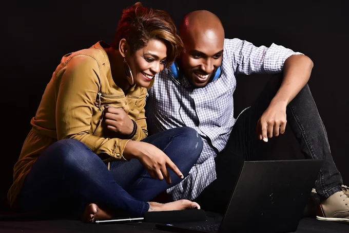 Foto de um homem e uma mulher sentados no chão assistindo vídeo no notebook