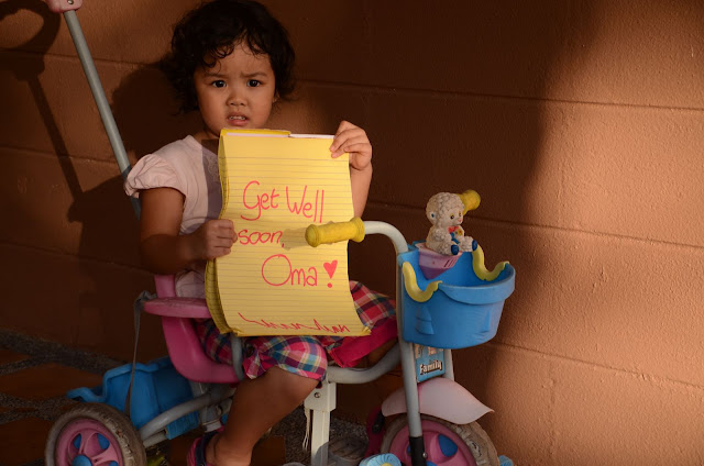 Kecil holding yellow pad with writing: Get well soon, Oma!