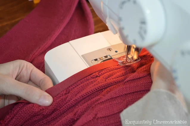 Running a sweater through the sewing machine to attach ribbon to sweater