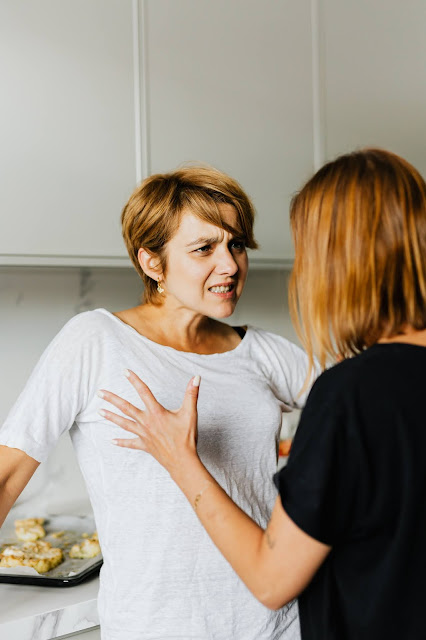 Two woman arguing with each other with the white one wanting to stop being critical with other.