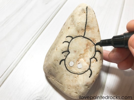 drawing the outline of the halloween spider onto the rock stone with a black posca pen
