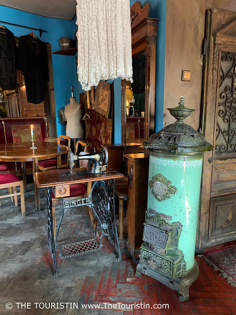 A Singer sewing machine, a bright green period masonry heater, red upholstered chairs, a red sofa and parts of an ancient-looking wooden ornamented door.