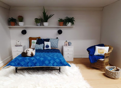 1/12 scale modern miniature bedroom in blue and white, with a cane chair in the corner next to a basket of knitting.