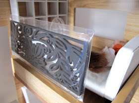 A laser-cut wooden bookmark-sized black panel leaning on the top of a one-twelfth scale doll's house mezzanine wall.