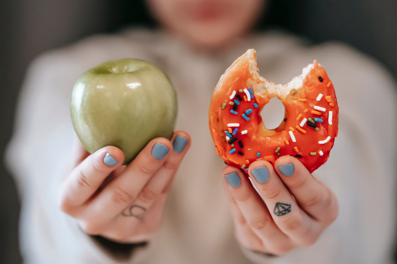 a close-up picture of two hands which are holding an apple in one hand and bitten donut in another