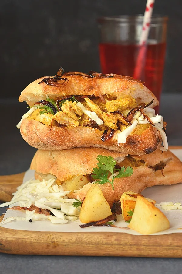A wooden board with leftover chicken curry sandwich,served with cold beverage and caramelized onions and butters potato chunks