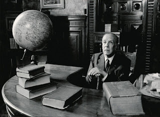 Jorge Luis Borges sitting at his table, surrounded by books.