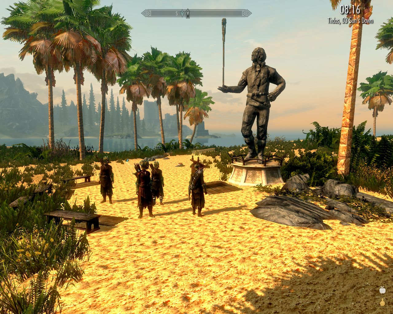 Laura and followers stand on the sand in front of a large statue of a man who balances a stick on his palm