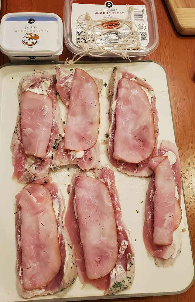 this is pork stuffed with ham and cream cheese, herbs and spices on a cutting board