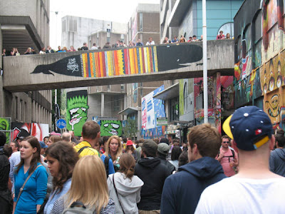 Crowds walking between concrete walls that have been painted with brightly colored graffiti-style images, varying greatly