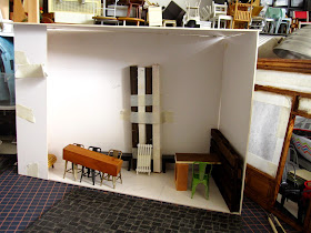 Modern dolls' house miniature cafe, half built with furniture arranged in a cardboard room.