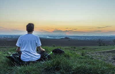 Hombre joven colocado de espalda, meditando al aire libre en un atardecer; en un hermoso paisaje mirando al horizonte.