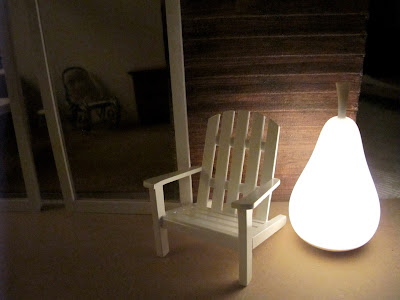 Dry fit of a dolls' house shed kit at night, with an Adirondack chair and a light-up pear sculpture outside it.