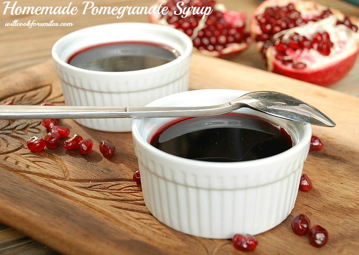 Pomegranate syrup in to ramekins with a spoon over one on a cutting board with pomegranate seeds 