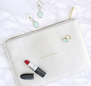 white clutch bag with red lipstick and earing on flat lay