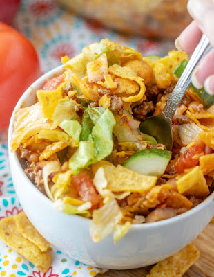 Frito salad is a fun twist on a taco salad. It is loaded with flavor and is perfect for potlucks, but also makes a fun dinner main dish. The homemade catalina salad dressing is easy to make and the salad is packed full of goodies. fork getting a bite of frito taco salad
