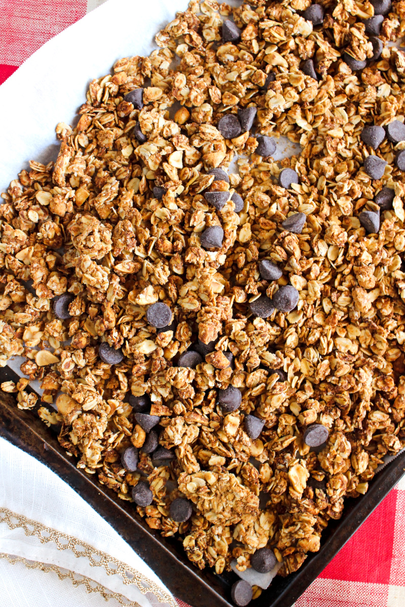 Chocolate Chip Peanut Butter Granola | The Two Bite Club Chocolate Chip Peanut Butter Granola on a parchment-lined baking sheet on a red and white checkered background.