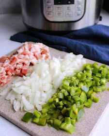 cutting board filled with chopped bacon, onions and green pepper in front of instant pot for maple baked beans