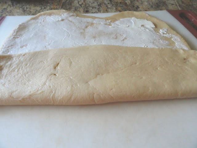 Cinnamon Roll dough spread with cream cheese and being folded into 3rds.